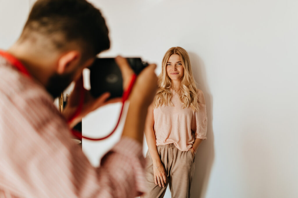 Dark-haired guy makes photo of his blond girlfriend dressed in pink T-shirt and beige pants against