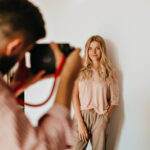 Dark-haired guy makes photo of his blond girlfriend dressed in pink T-shirt and beige pants against