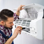 Happy Male Technician Repairing Air Conditioner With Screwdriver