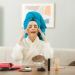 with-closed-eyes-young-girl-wrapped-hair-towel-applying-tone-up-cream-sitting-table-with-makeup-tools-living-room (1)