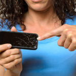 Close up of one woman in blue shirt holding broken mobile phone in her hands