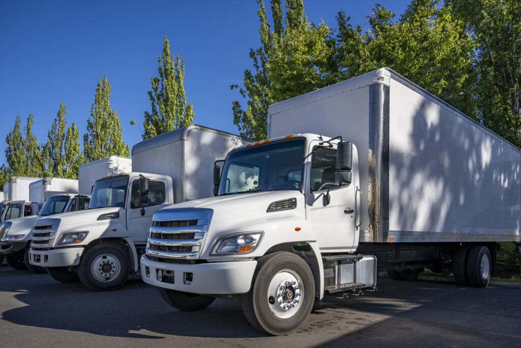 Middle duty day cab rig semi trucks with box trailers standing in row on the warehouse industrial parking lot at sunny day