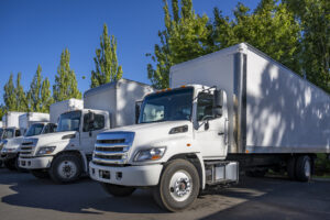 Middle duty day cab rig semi trucks with box trailers standing in row on the warehouse industrial parking lot at sunny day