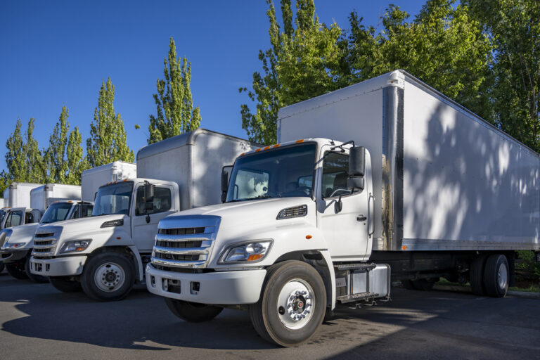Middle duty day cab rig semi trucks with box trailers standing in row on the warehouse industrial parking lot at sunny day