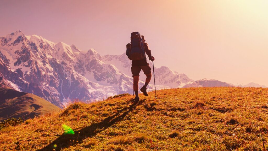 Hiker using walking sticks for hiking on mountain trail at sunrise