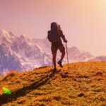 Hiker using walking sticks for hiking on mountain trail at sunrise