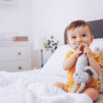 Baby boy sitting in bed and playing with stuffed animal toys