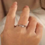 Delicate silver Infinity Ring with sparkling diamonds worn on a woman's finger symbolizing eternal love and emotional connection.