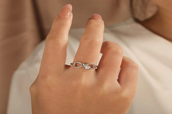 Delicate silver Infinity Ring with sparkling diamonds worn on a woman's finger symbolizing eternal love and emotional connection.