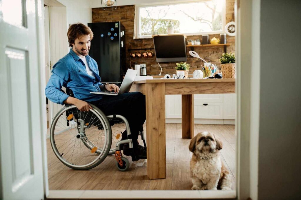 happy-businessman-wheelchair-looking-his-dog-while-working-laptop-home (1)