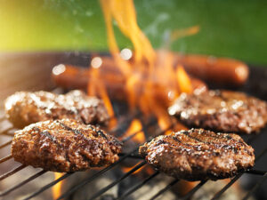 hamburgers and hotdogs cooking on flaming grill shot with selective focus