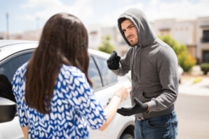 Masked man pointing a gun at a woman during an armed robbery near a car
