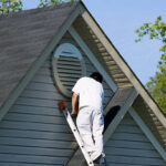 Painter working at the top of an extension ladder on a two story suburban home.
