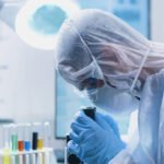 Researcher doctor with ppe equipment looking into medical microscope analyzing virus sample