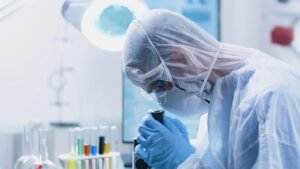 Researcher doctor with ppe equipment looking into medical microscope analyzing virus sample