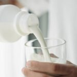 Close-up hand of man pouring milk into a glass.