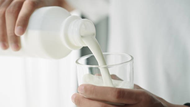 Close-up hand of man pouring milk into a glass.