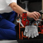 Professional plumber taking adjustable wrench from tool bag indoors, closeup