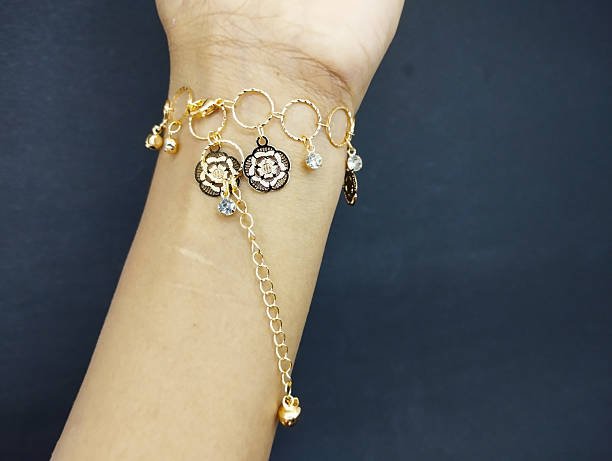 Gold chain bracelet with flower charms and small crystals on wrist.