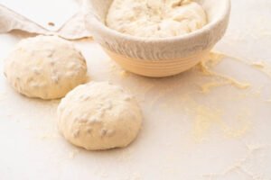 Baking bread. Dough in proofing basket on wooden table with flour. Top view.